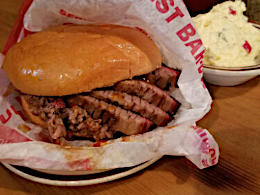 A BBQ brisket sandwich from Demeris BBQ in Houston, Texas. Some potato salad is in a bowl in the background.